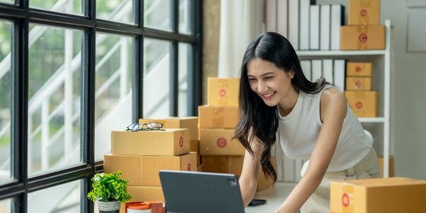 Online seller using a tablet at a desk surrounded by shipping boxes